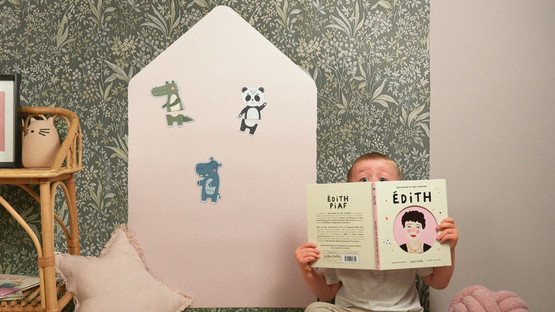 Un enfant dans une chambre avec un livre et un tableau magnétique maison colorée derrière lui