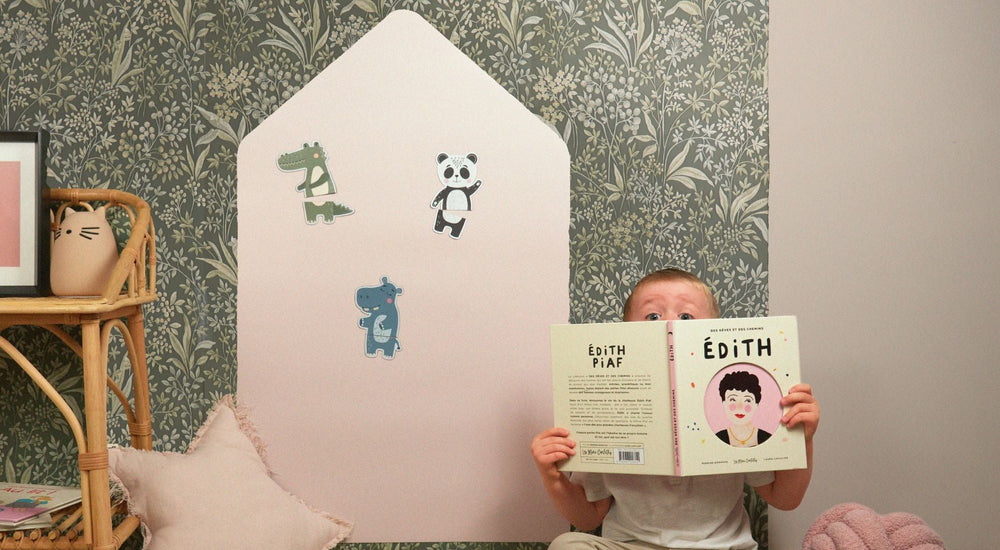 Un enfant dans une chambre avec un livre et un tableau magnétique maison colorée derrière lui