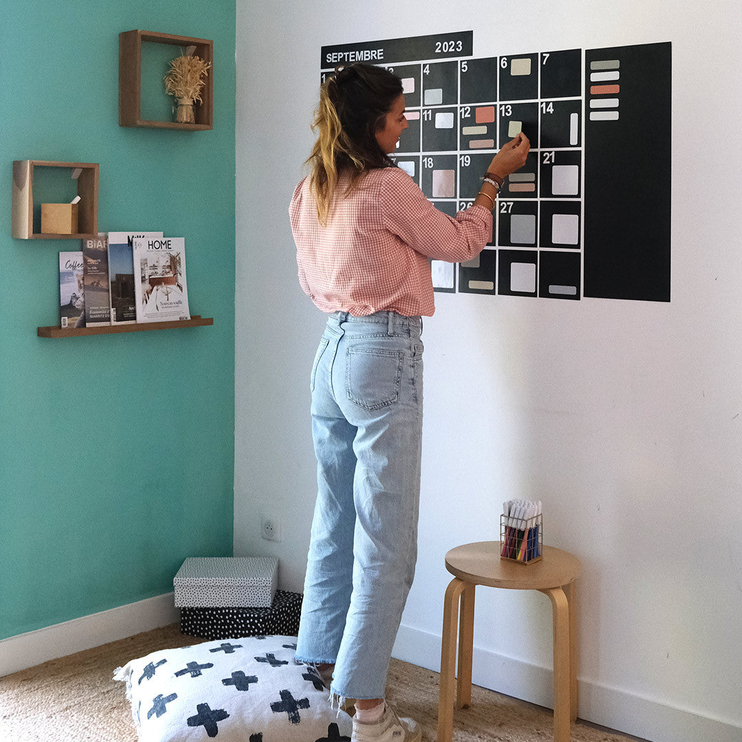 Femme installant un calendrier mural magnétique effaçable dans un salon