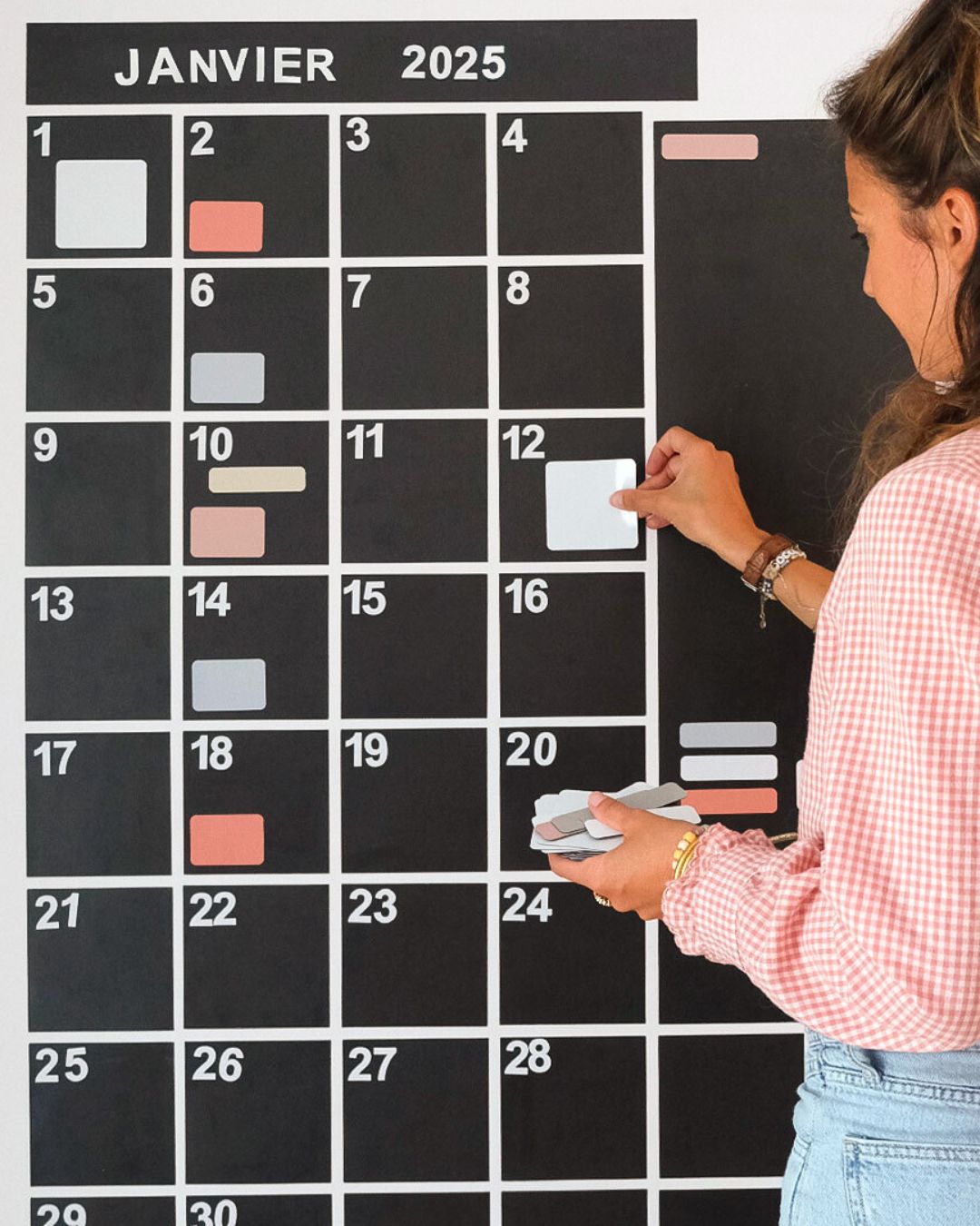 Femme utilisant un calendrier mural magnétique effaçable, planning mensuel de janvier