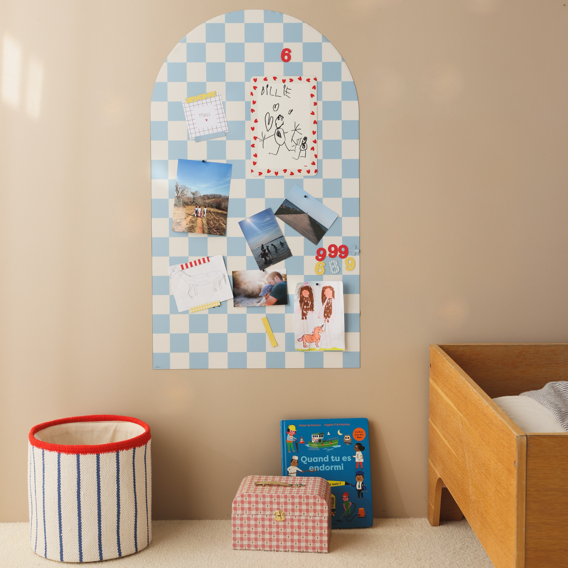 Tableau magnétique arche damier bleu dans une chambre d'enfant, avec dessins, photos et chiffres magnétiques.