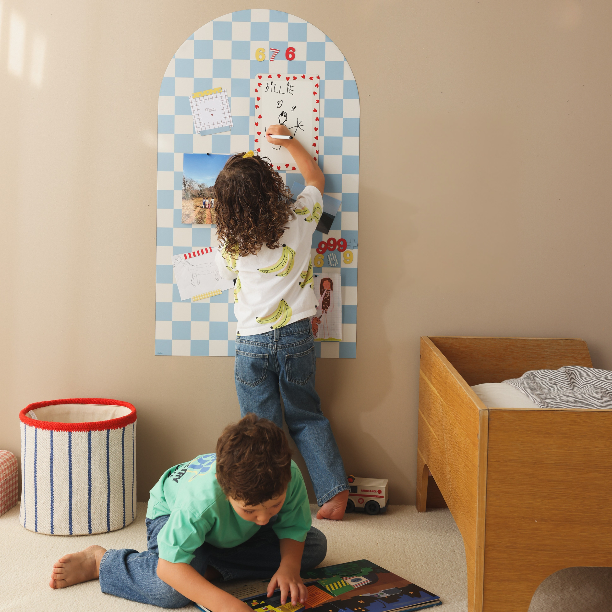 Petite fille écrivant sur une ardoise effaçable à sec petit coeur rouge, aimantée sur un tableau magnétique arche