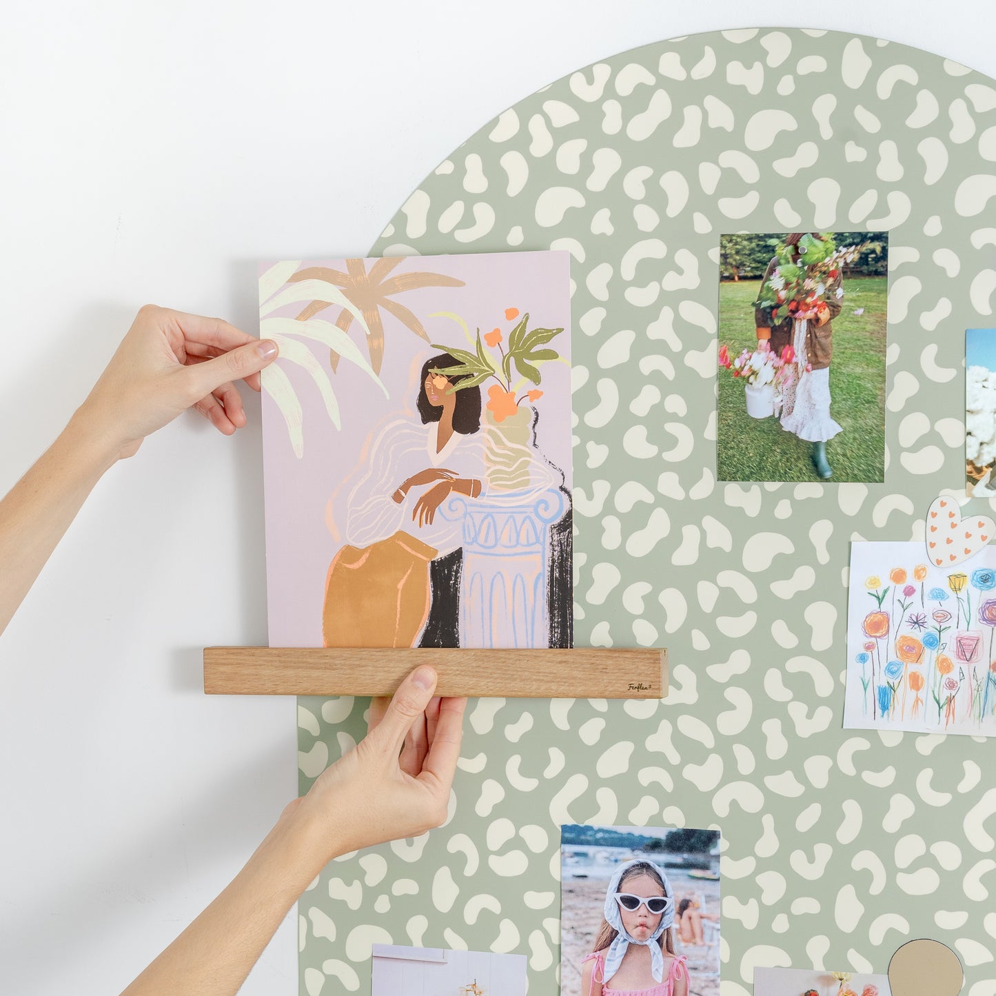 Mains tenant une affiche sur une étagère en bois aimantée sur un tableau magnétique mural à motifs léopard vert