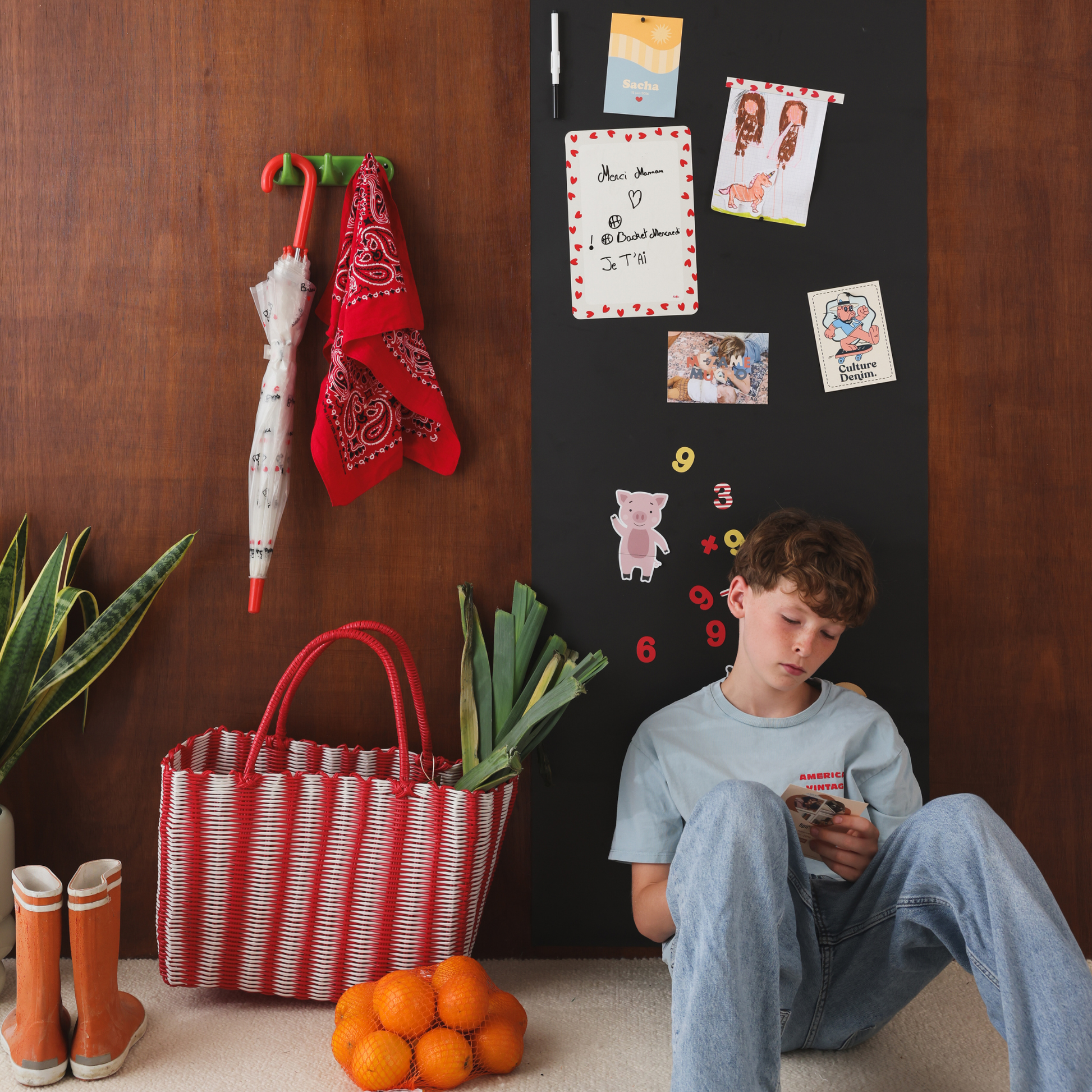Adolescent assis près d'un papier peint magnétique noir avec ardoise souple rectangle bordure petits coeurs rouges dans un décor d'entrée de maison