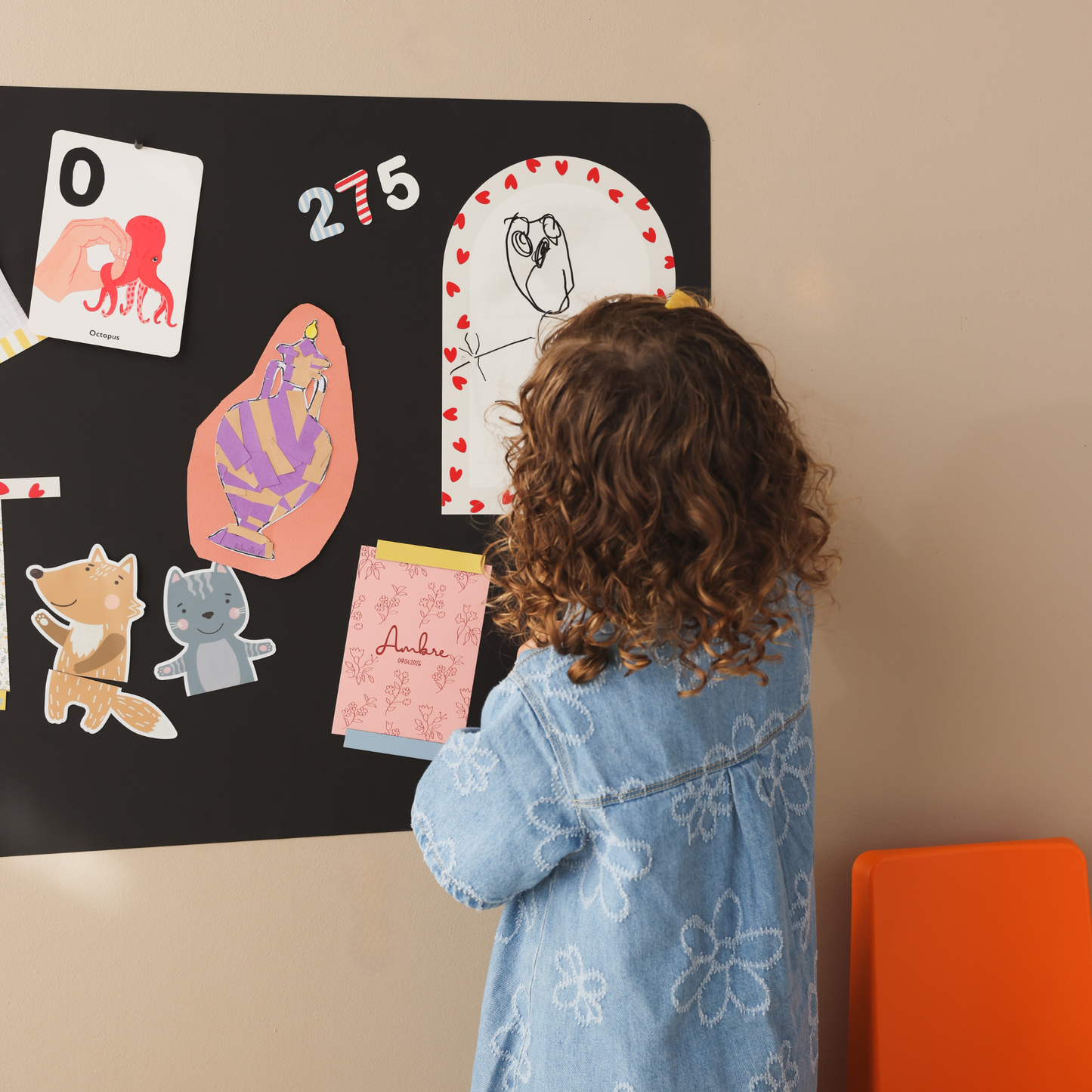 Petite fille dessinant au feutre noir effaçable à sec sur l'ardoise magnétique arche bordure petits coeurs rouges, aimantée sur un tableau magnétique rectangle avec des magnets chiffres et animaux pour enfant