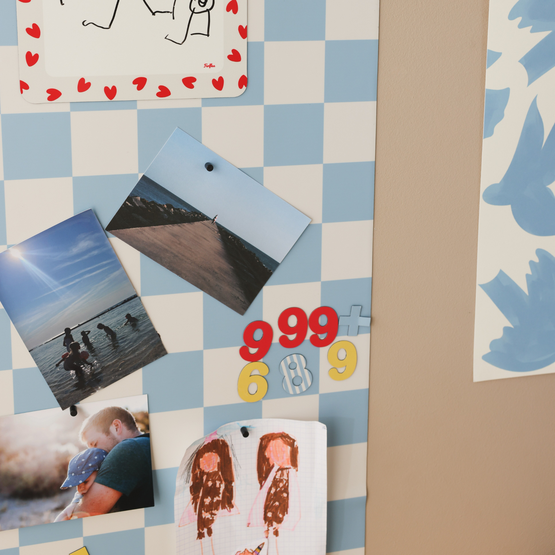 Chiffres magnétiques colorés sur tableau magnétique mural damier bleu Ferflex, avec photos de vacances et dessins d'enfant
