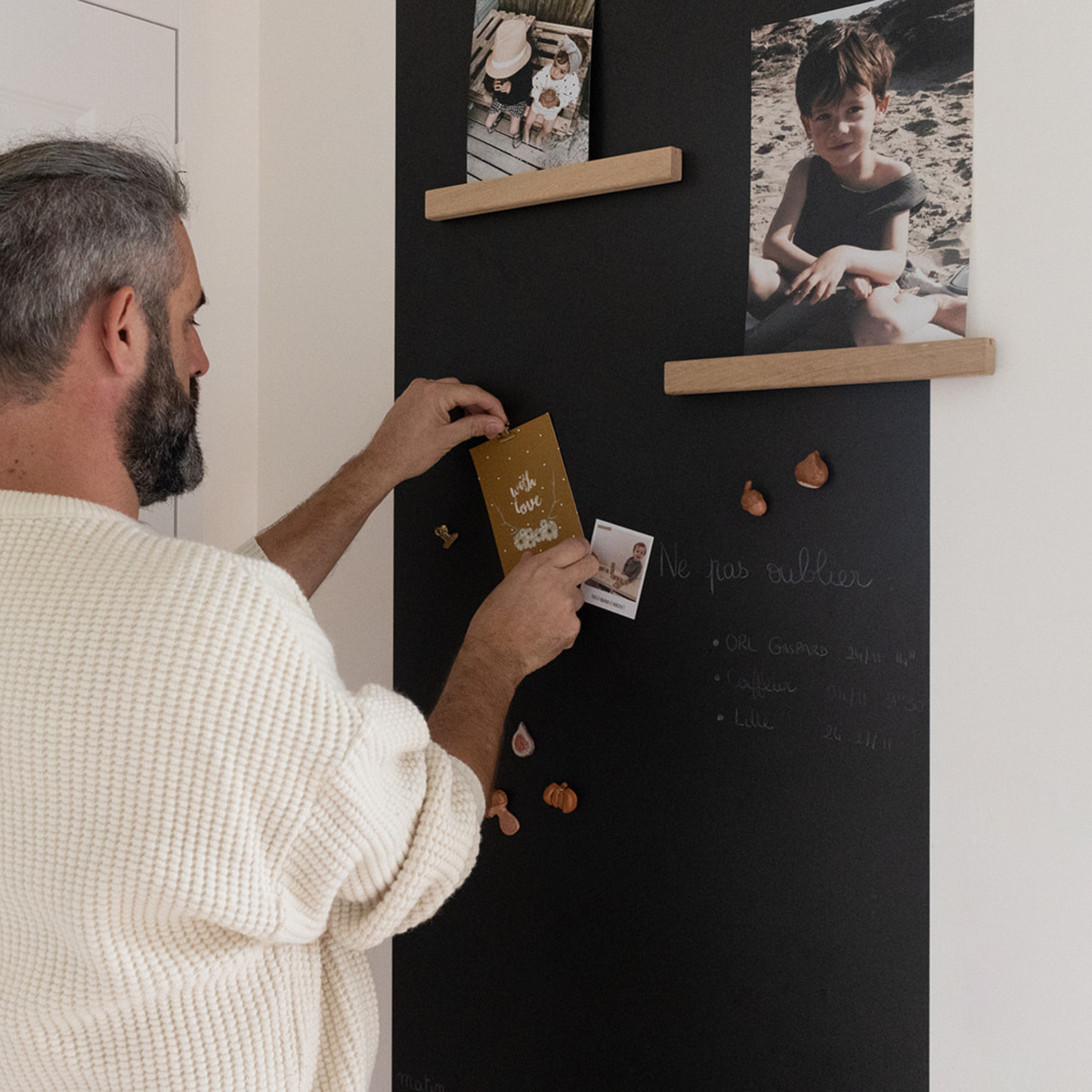 Homme accrochant photo sur tableau magnétique avec étagères en bois