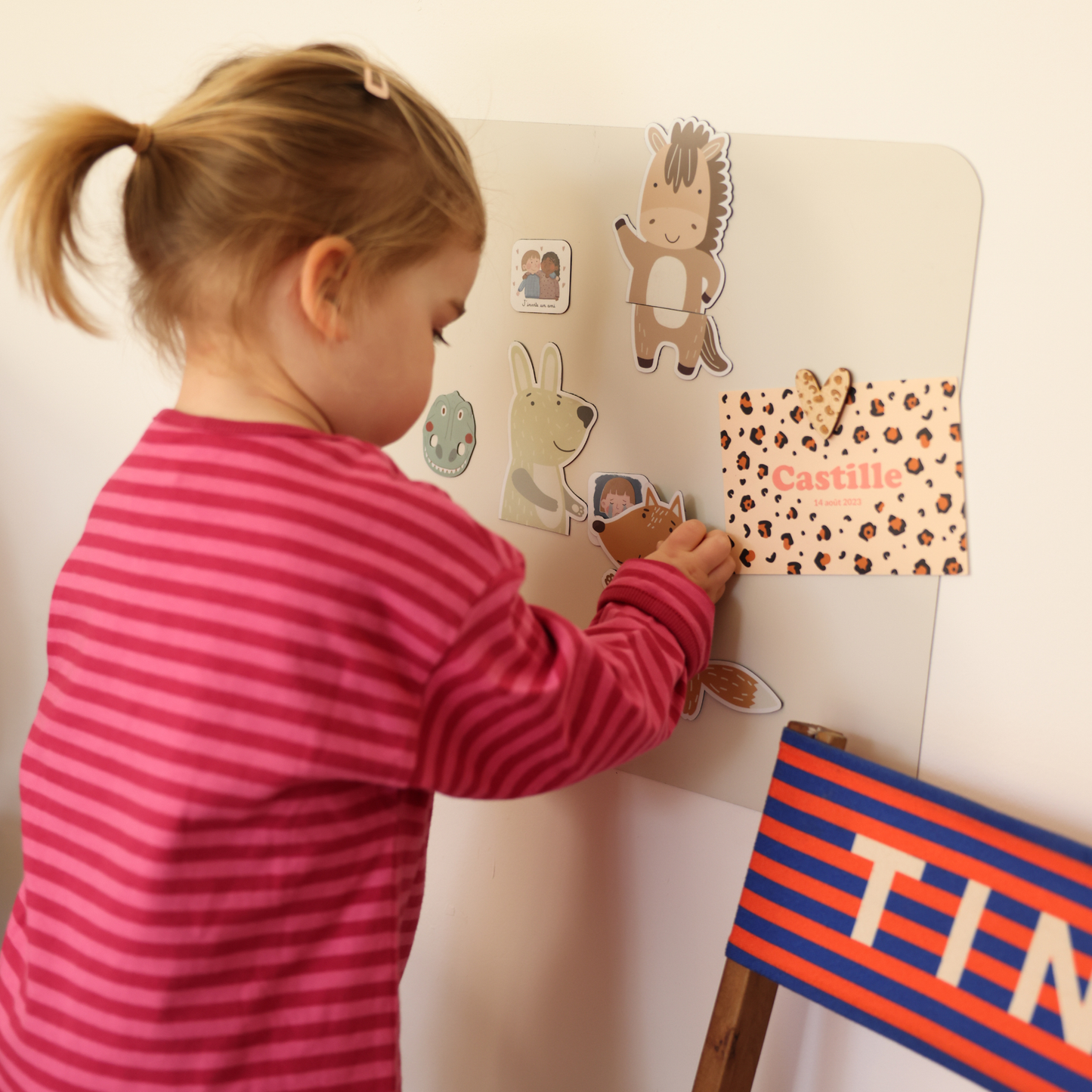 Enfant jouant sur un tableau mural magnétique avec des magnets animaux type puzzle et des magnets routines du quotidien